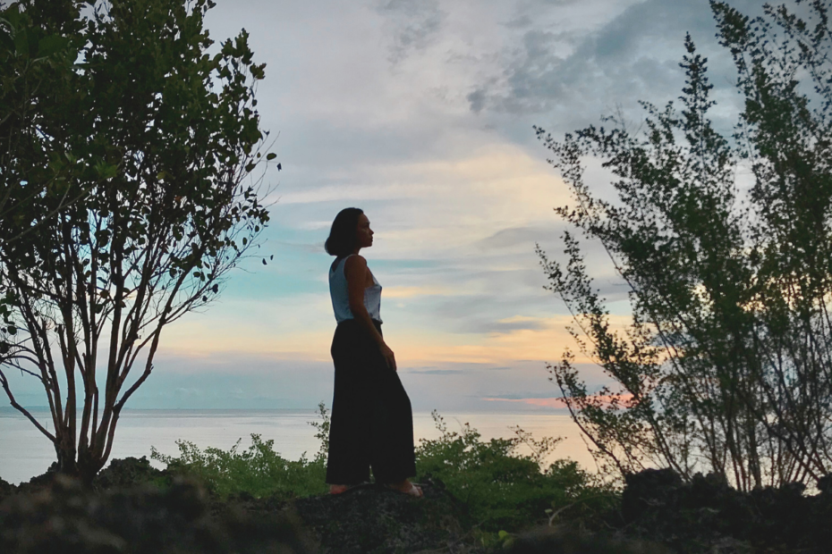 Lady standing on a cliff with a beautiful sunset view of the ocean