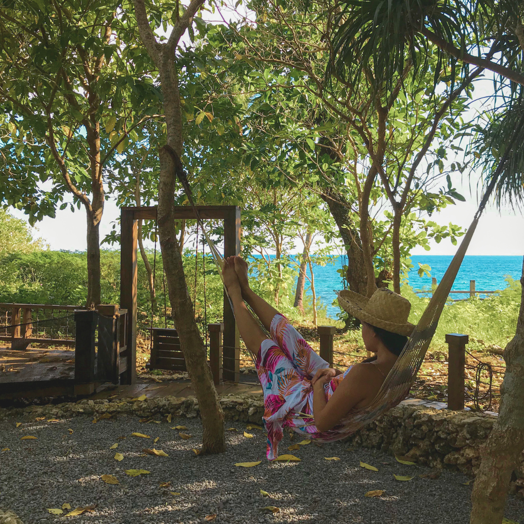 Lady on a hammock in a peaceful, serene environment surrounded by nature, lush green trees, and the blue ocean.