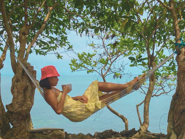 Woman drinking coffee on a hammock overlooking the ocean enjoying some me-time
