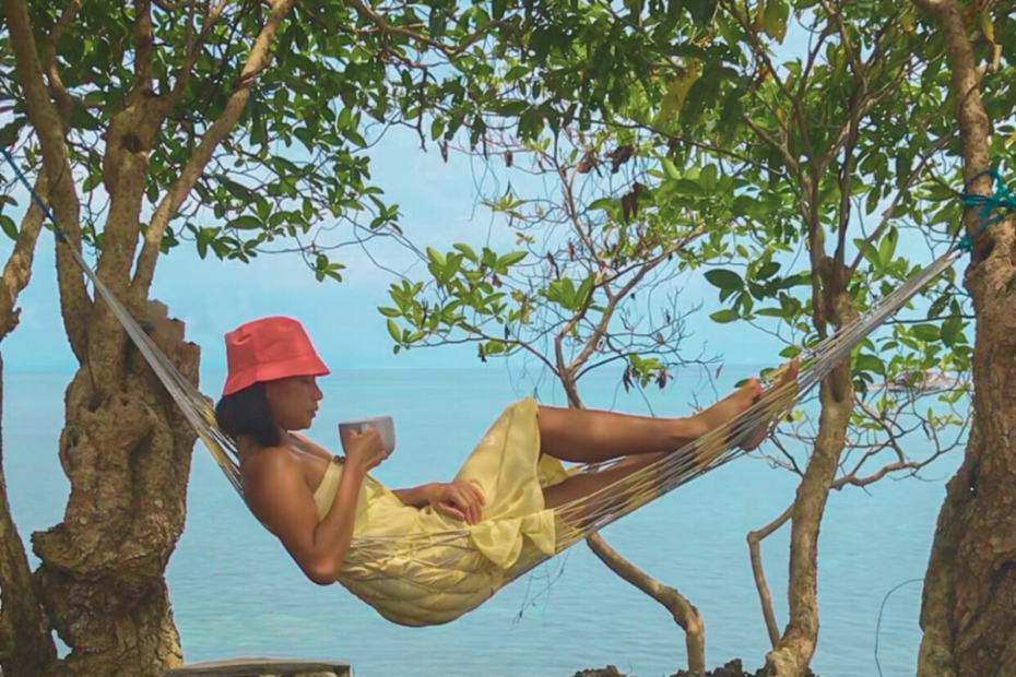 Woman drinking coffee on a hammock overlooking the ocean enjoying some me-time