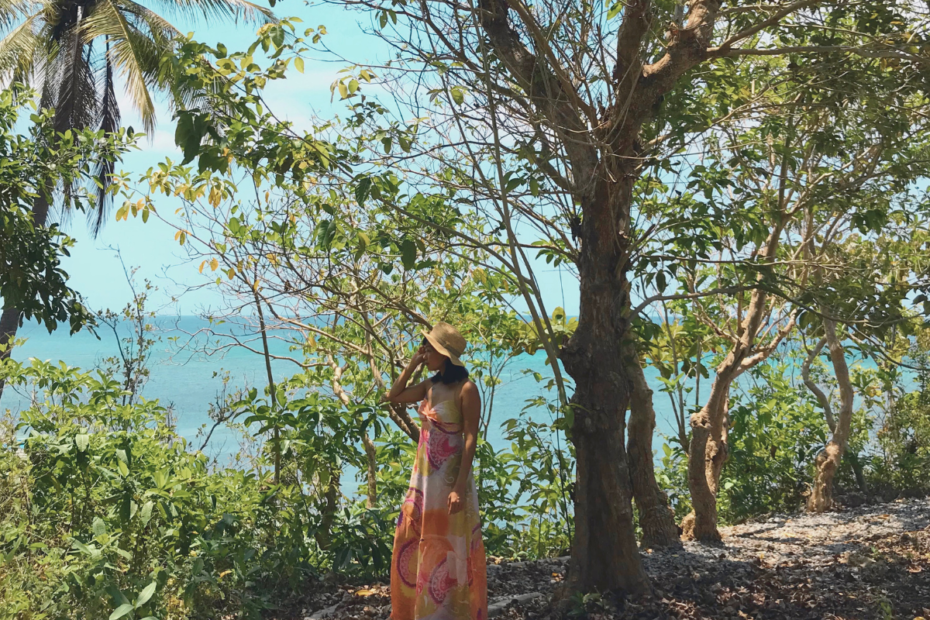 A woman stading under a tree with a background of nature and the sea