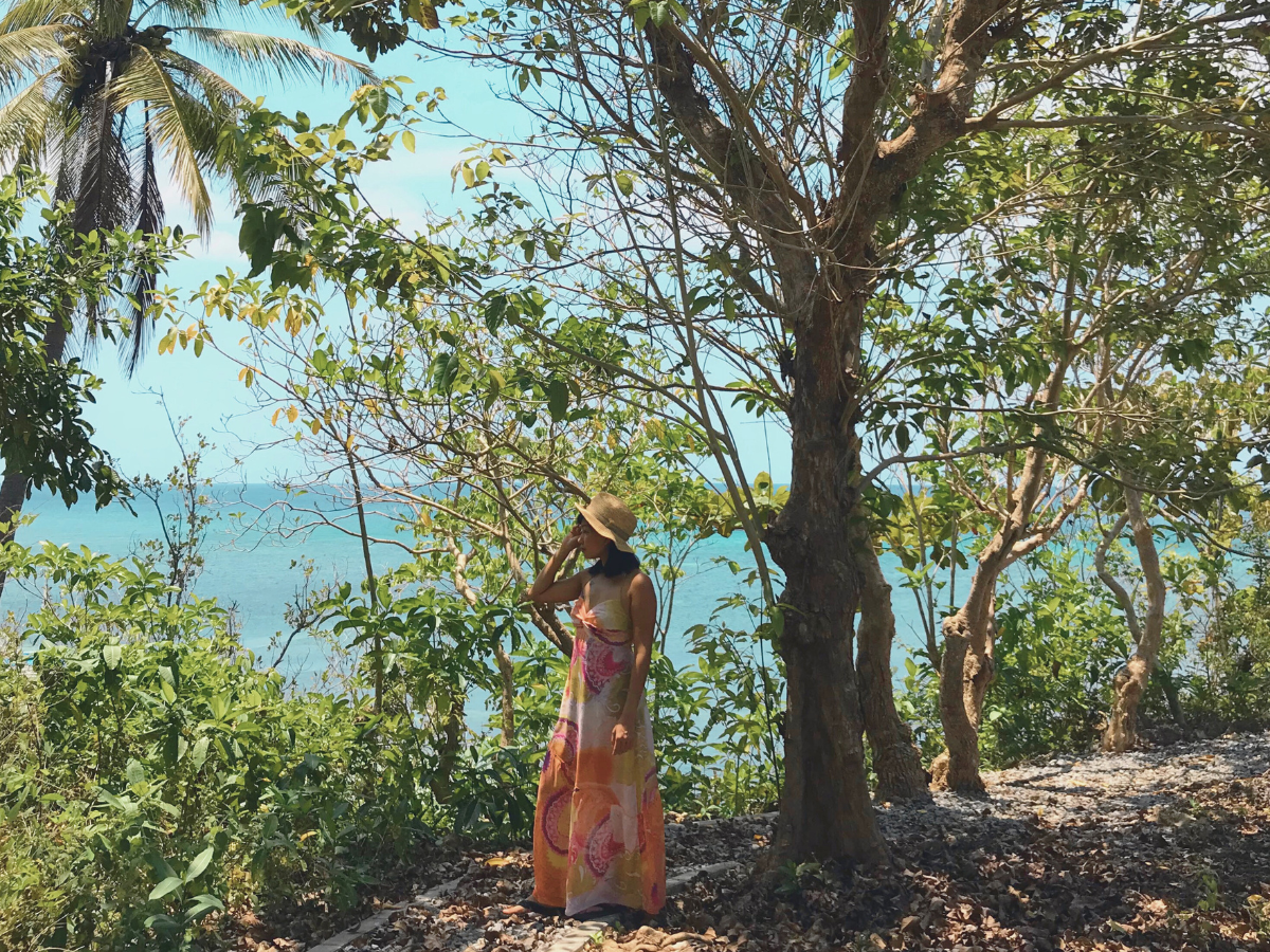 A woman stading under a tree with a background of nature and the sea