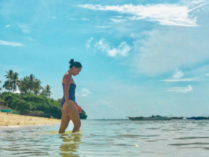 Woman walking on the beach with a clear, blue sky, thinking about sharing simple Self-Care Tips for moms