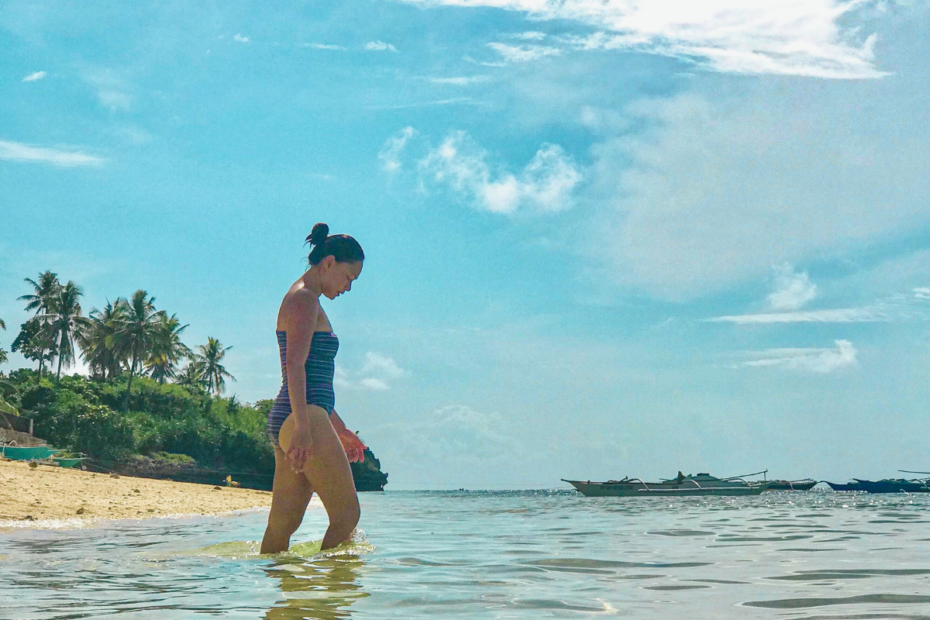 Woman walking on the beach with a clear, blue sky, thinking about sharing simple Self-Care Tips for moms