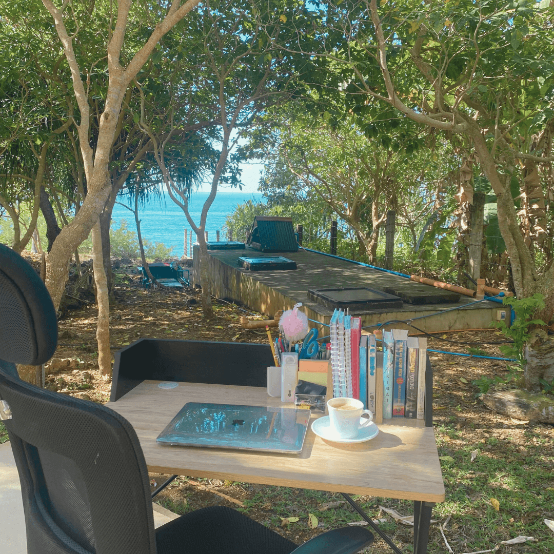 A working table with books and a laptop and office chair with a view of nature and the ocean