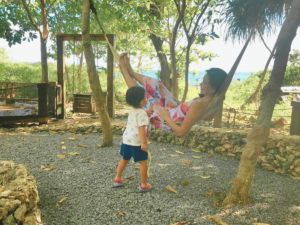 A mother relaxing on a hammock under the trees, playing with her daughter, reflecting on the journey of how she lost herself and found peace in nature.
