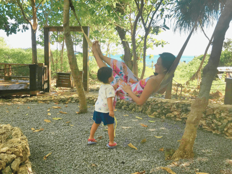 A mother relaxing on a hammock under the trees, playing with her daughter, reflecting on the journey of how she lost herself and found peace in nature.