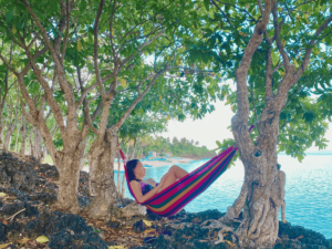 A mother relaxes on a hammock, enjoying some 'me-time' as she gazes over the ocean, surrounded by lush nature.
