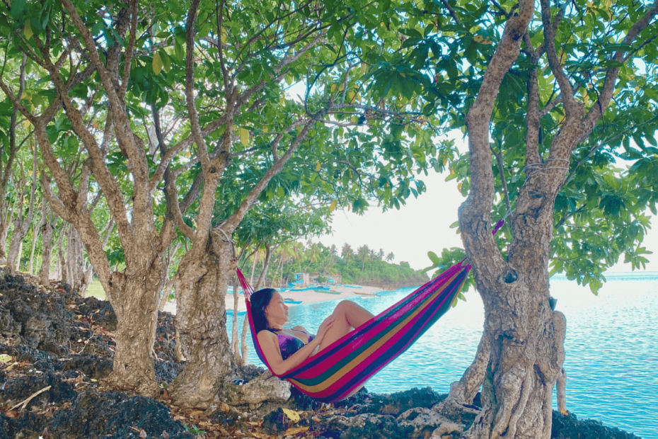 A mother relaxes on a hammock, enjoying some 'me-time' as she gazes over the ocean, surrounded by lush nature.