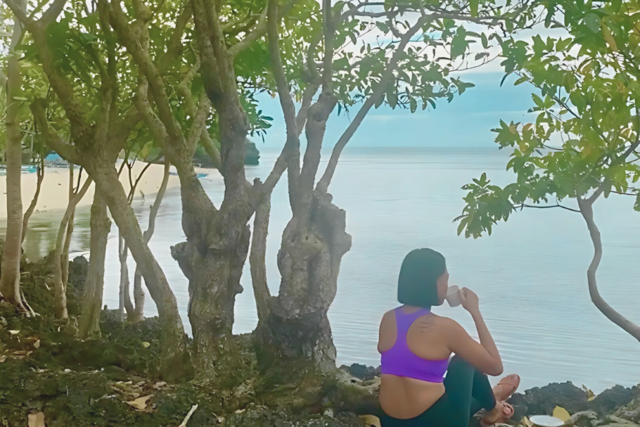 Woman sitting by a cliff, gazing out at the ocean while drinking her morning coffee, embracing the calmness of the moment and practicing mindfulness.