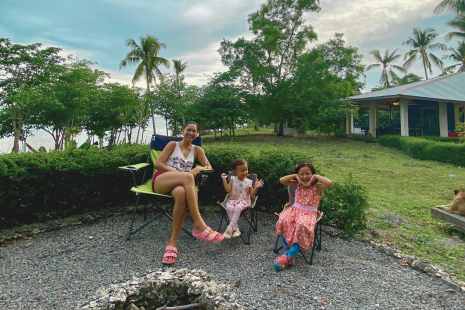 Mother and her two daughters sitting on picnic chairs, smiling and looking at the camera, enjoying a peaceful moment before the sun sets to start a bonfire—perfect example of listening more and connecting as a family.