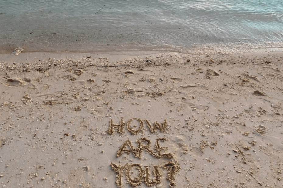 "How are you?" text written on the sand on the beach during sunset