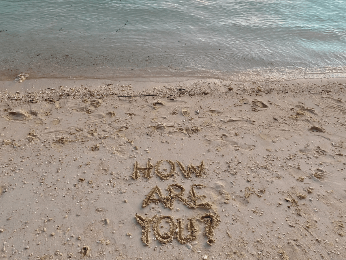 "How are you?" text written on the sand on the beach during sunset