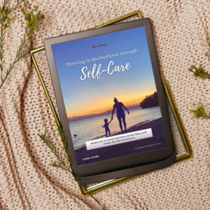 An ebook titled 'Thriving in Motherhood through Self-Care: A Transformational Ebook Journal for Moms' displayed on a tablet. The cover features a serene beach sunset with the silhouette of a mother holding her child’s hand, symbolizing connection and peace. The tablet rests on a cozy beige knit blanket, surrounded by sprigs of greenery for a warm, inviting aesthetic.