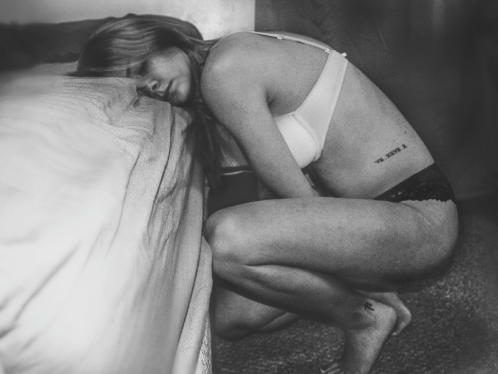 A woman in a lingerie leaning against the bed recovering from birth
