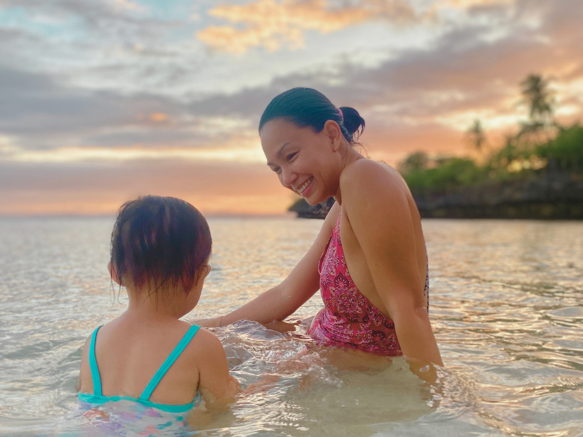 A mom smiling at her daughter enjoying the sunset at the beach, reflecting her healing in motherhood journey.