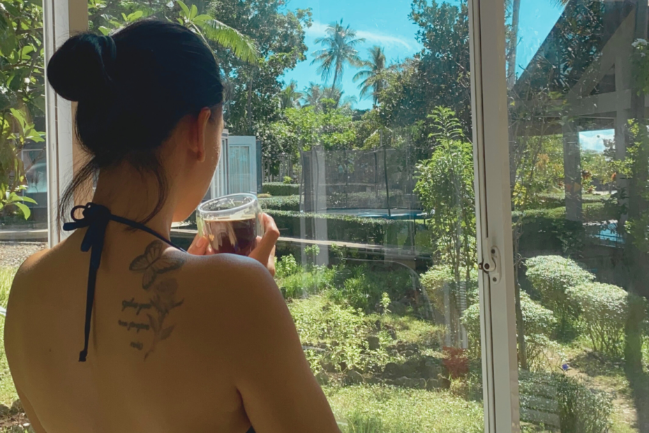 A mom sipping coffee in her kitchen, pausing to watch nature through the window and practicing gratitude for the quiet moment.