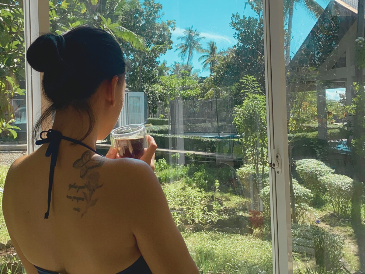 A mom sipping coffee in her kitchen, pausing to watch nature through the window and practicing gratitude for the quiet moment.