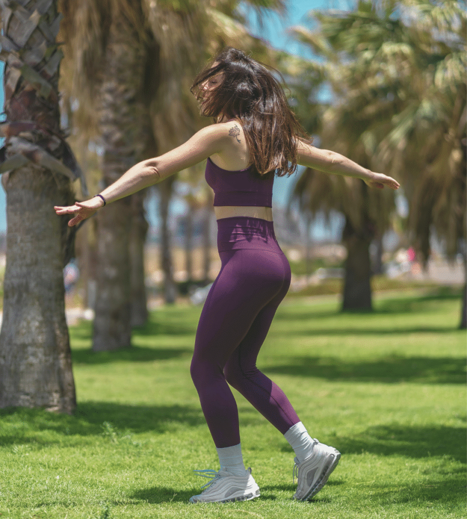 A woman on a workout clothes dancing on grass feeling more than just mom practicing holistic self-care for moms