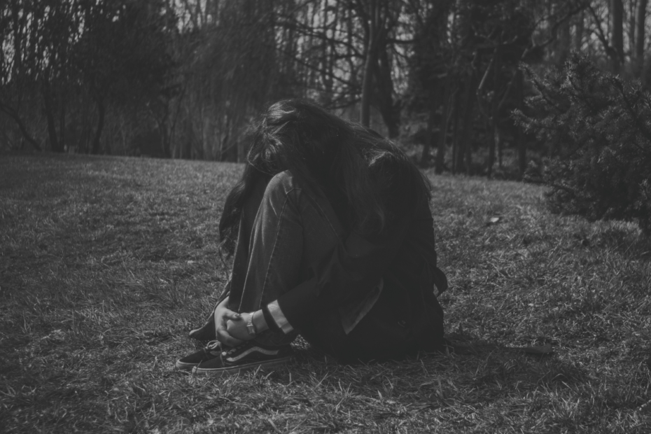 Woman curled up on the grass illustrating the mental health effects of a toxic relationship.