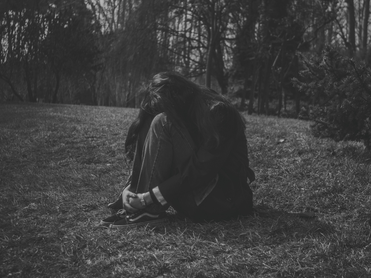 Woman curled up on the grass illustrating the mental health effects of a toxic relationship.